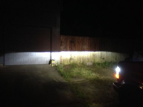 1992 Ford F-150 - A truck's bright headlight beam cuts through the darkness, illuminating a garage door and a wooden fence.