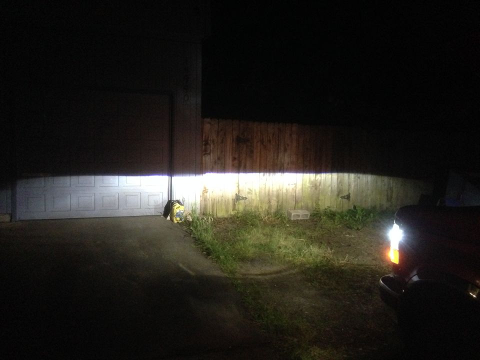 Truck headlight beam illuminating a garage door and wooden fence at night