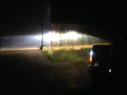 1992 Ford F-150 - A vehicle's headlights are on, casting a bright beam across a driveway and garage door at night.