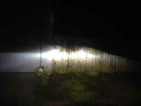 1992 Ford F-150 - The bright beam from a vehicle's headlights illuminates a wooden fence and a garage door in the darkness.