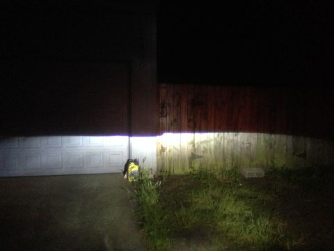 1992 Ford F-150 - The bright beam of headlights is cast onto a garage door and a weathered wooden fence, illuminating the night scene.