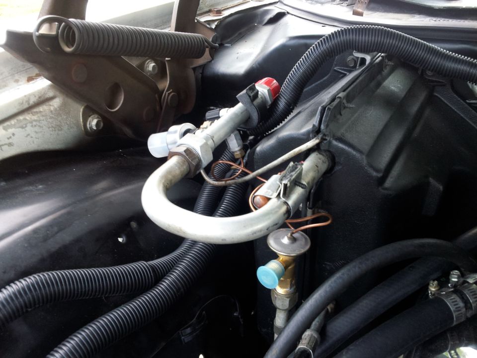 Air conditioning lines and hoses in engine bay, with visible springs and black corrugated tubing
