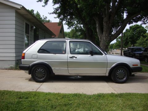 1985 Volkswagen GTI - A silver 1985 Volkswagen GTI is parked on a concrete driveway in front of a house.