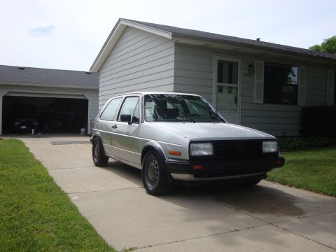 1985 Volkswagen GTI - A silver Volkswagen Golf Mk2 is parked on a concrete driveway in front of a suburban house.