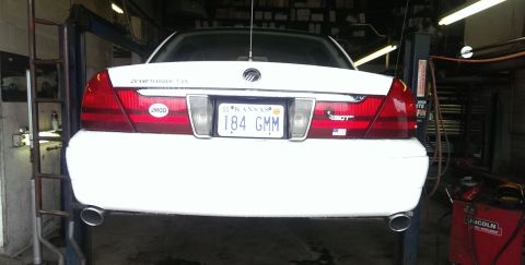 2000 Mercury Grand Marquis - Rear view of a white 2000 Mercury Grand Marquis lifted in a garage, displaying its taillights and license plate.