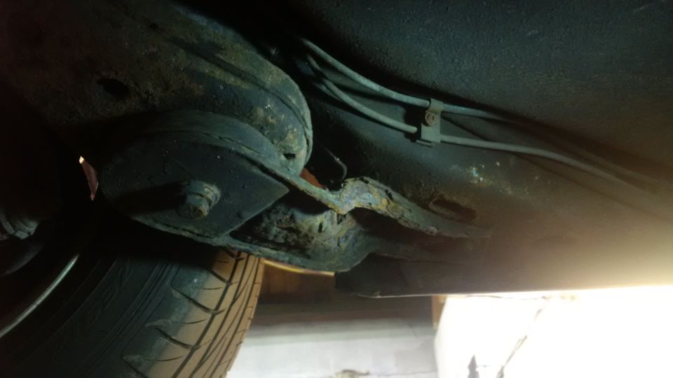 Undercarriage of a vehicle showing extensive rust on the frame and suspension components, with a tire visible