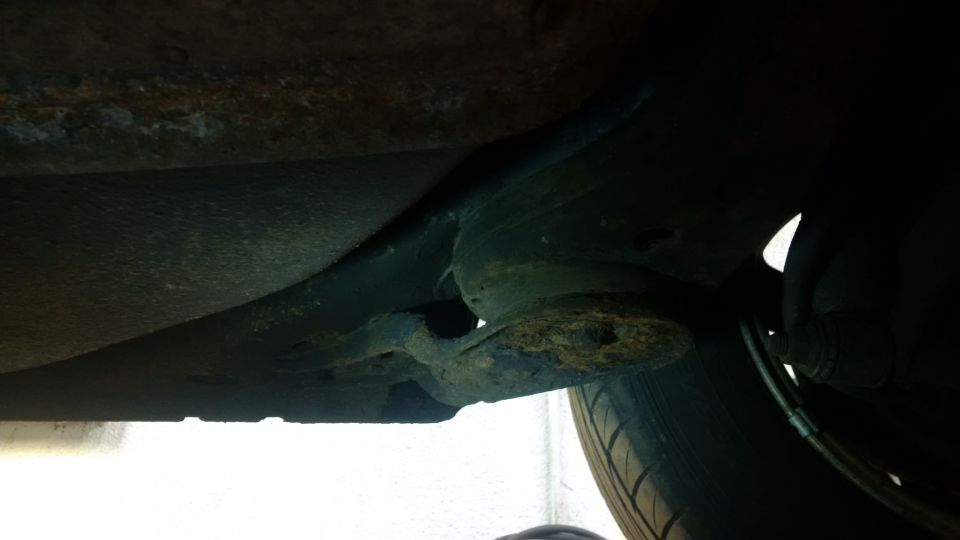 Undercarriage view of rusted metal and suspension components, with a tire visible