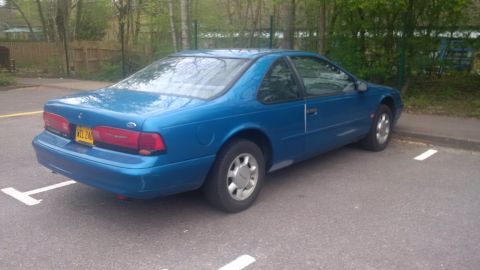 1994 Ford Thunderbird - A blue 1994 Ford Thunderbird is parked in a lot, showing its rear and side profile.