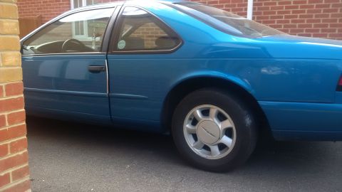 1994 Ford Thunderbird - A blue coupe is parked outdoors, partially obscured by a brick structure. The vehicle's side profile is visible.