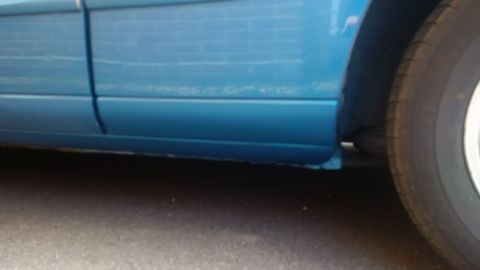 1994 Ford Thunderbird - Close-up of a blue car's side panel showing evidence of rust repair and a tire.