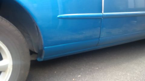 1994 Ford Thunderbird - Close-up of a blue car's side panel, showing the door seam and wheel well area.