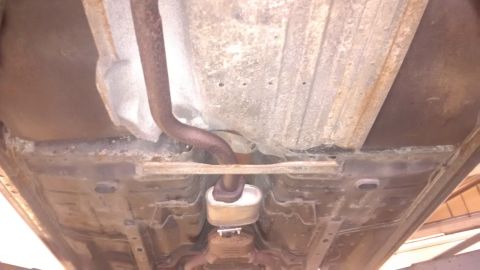 1994 Ford Thunderbird - The underside of a vehicle displays significant rust and an exhaust system component.
