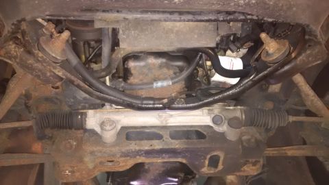 1994 Ford Thunderbird - Underside view of a vehicle's steering rack and engine oil pan, showing significant rust and grime.