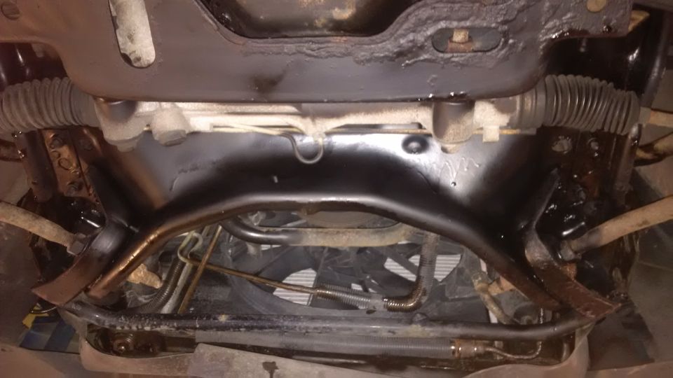 Underside view of vehicle's front suspension and steering components, showing rust and undercoating
