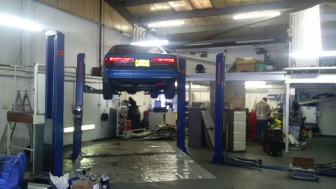 1994 Ford Thunderbird - A blue 1994 Ford Thunderbird is raised on a lift inside a workshop for repairs.