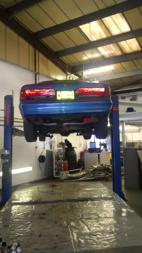 1994 Ford Thunderbird - The rear of a blue coupe is visible as it's raised on a car lift in a workshop.