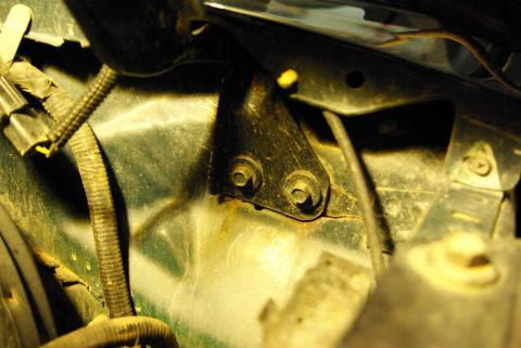 1995 Ford Bronco - Close-up view of a green hood hinge bracket, showing mounting bolts and wiring.