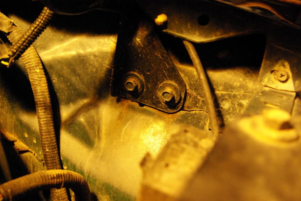 Close-up of a metal bracket with two bolts, next to a ribbed wiring harness in an engine bay