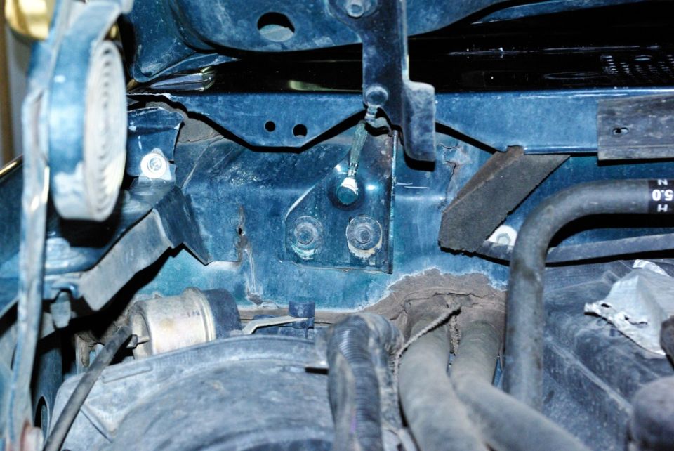 Close-up of engine bay with hoses and metal brackets visible. Some rust is present