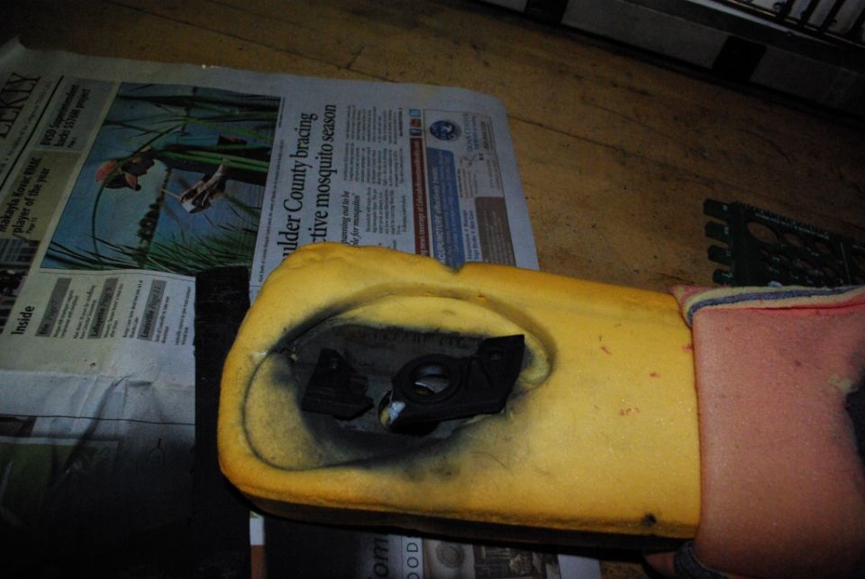 Car seat foam with a black plastic component inside, resting on newspaper