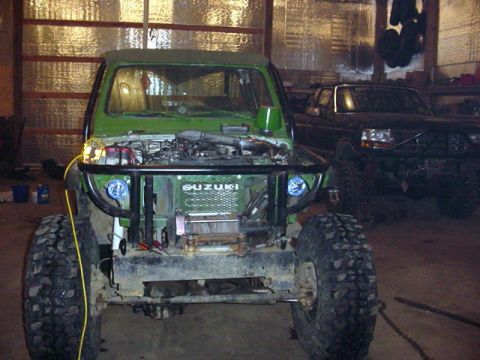 1992 Ford Bronco - A green Suzuki Samurai is parked in a garage next to a dark-colored truck.