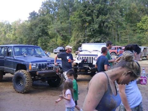 Blue Jeep Cherokee XJ with winch, white Jeep Wrangler, and other off-roaders gathered on a dirt path