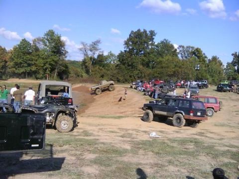 Off-road vehicles gathered on a dirt lot with trees in the background