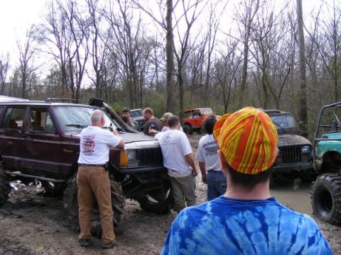Several off-road vehicles, including a maroon Jeep Cherokee and a black Jeep Wrangler, are in a muddy area wit