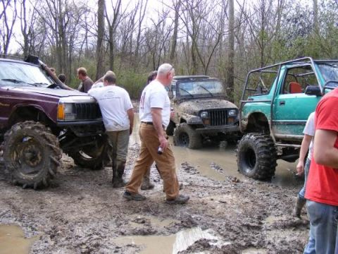 Several modified off-road vehicles stuck in thick mud with people around them