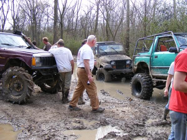 Several modified off-road vehicles stuck in thick mud with people around them