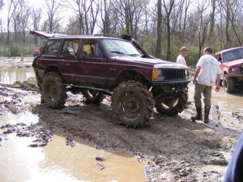Maroon Jeep Cherokee XJ with oversized tires in mud