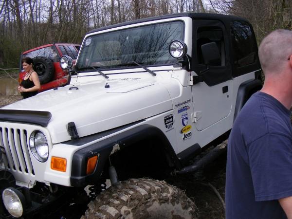 White Jeep Wrangler with black soft top, mud on tires. Red Jeep visible behind it