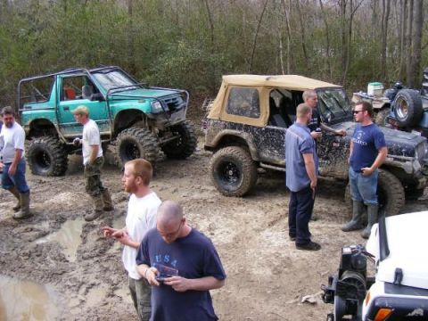 Green off-road SUV with large tires and a black Jeep with a tan top in mud