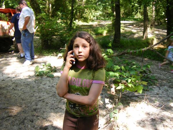 Girl talking on cell phone in wooded area with two men and an orange tractor