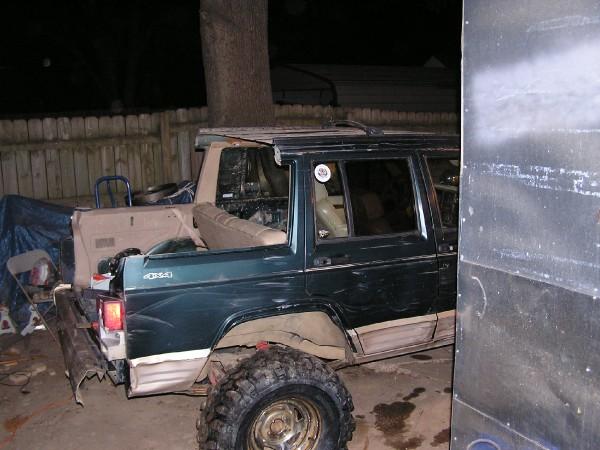 Green Jeep Cherokee XJ with a tan interior, parked next to another vehicle. The rear of the Jeep is visible