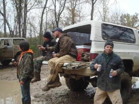 White SUV rear view with people in the bed, muddy terrain