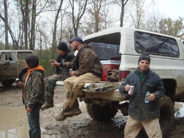 White SUV rear view with people in the bed, muddy terrain