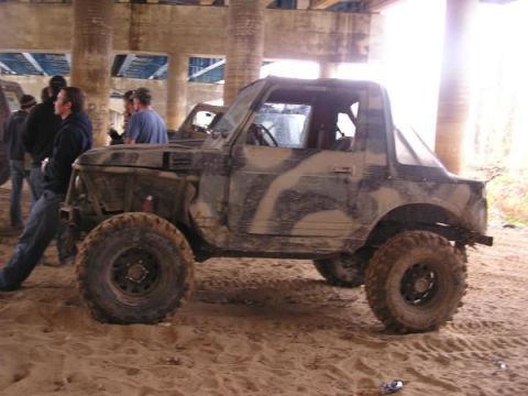 Muddy camouflage SUV parked on sand under a bridge