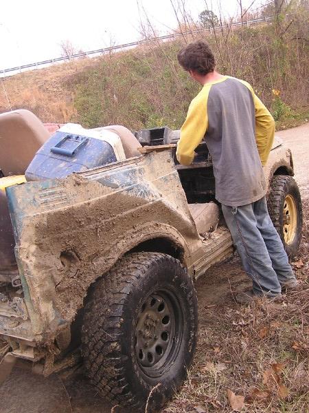 Muddy off-road vehicle with a person standing next to it, looking into the open top