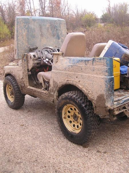 Mud-covered off-road vehicle with hood open, missing doors, and exposed interior