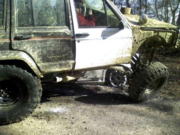 Muddy Jeep Cherokee XJ with large tires, driver visible inside
