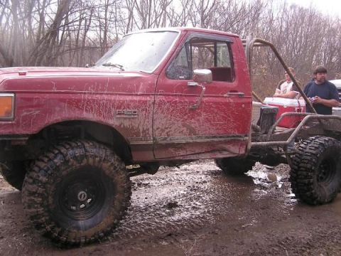 Red pickup truck with roll cage and large tires in mud