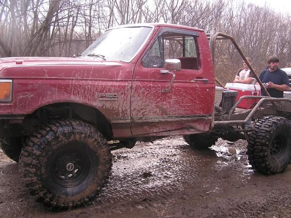 Red pickup truck with roll cage and large tires in mud