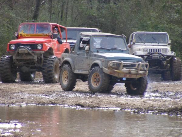 Four modified off-road vehicles in a muddy area