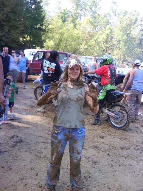 Mud-covered woman with hands up, dirt bikes and people in background