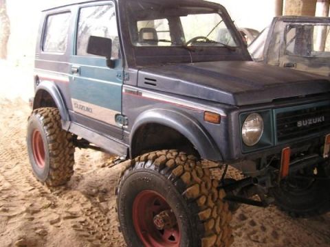Suzuki Samurai with large off-road tires, dark blue and teal paint, red rims