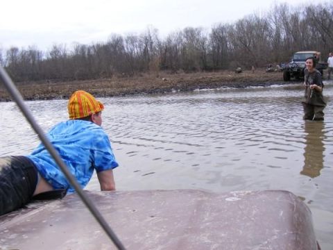 Person on vehicle hood in water with off-road vehicles in background
