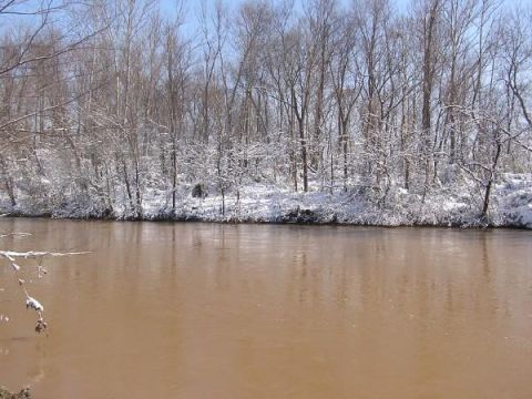 snowy trees line a muddy river under a clear sky. Supermotors.net logo in lower right