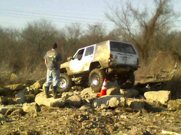 White Jeep Cherokee XJ on rocks with a person watching