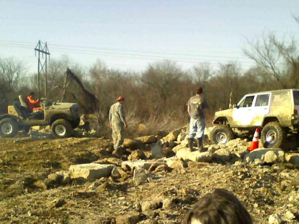 Off-road vehicles navigating a rocky terrain with three people present